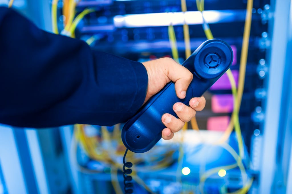 Home+ Close Up Of A Hand Holding A Telephone Receiver In A Server Room Emphasizing Technology. 19506332 1024x681